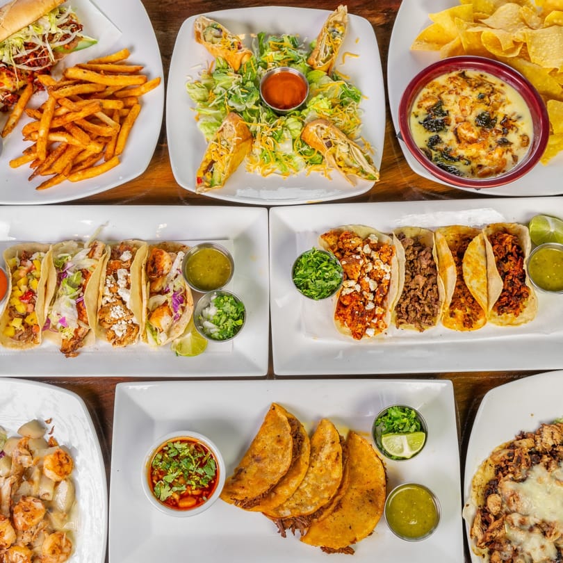 An overhead shot of various Mexican dishes, including tacos, quesadillas, fries, and dips.